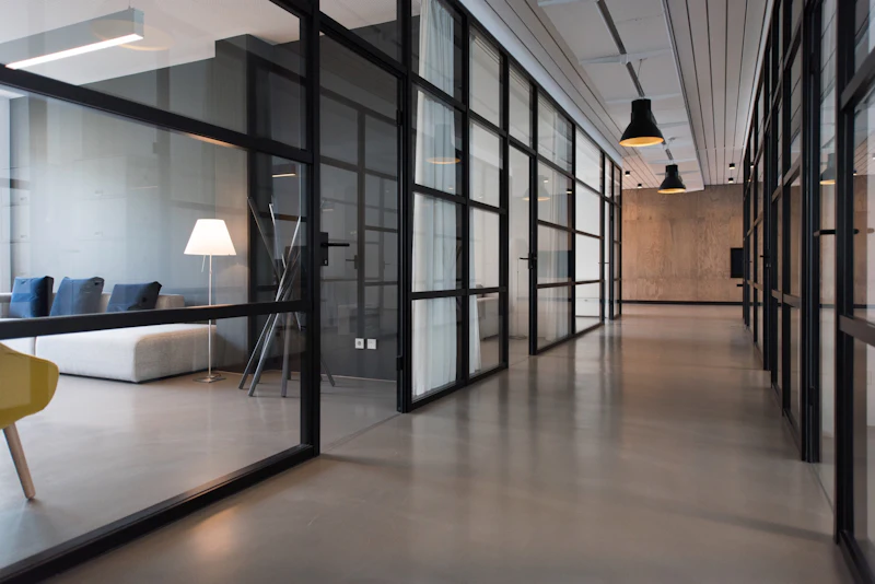 A glazed office corridor with black-framed partitions looking through to a meeting room
